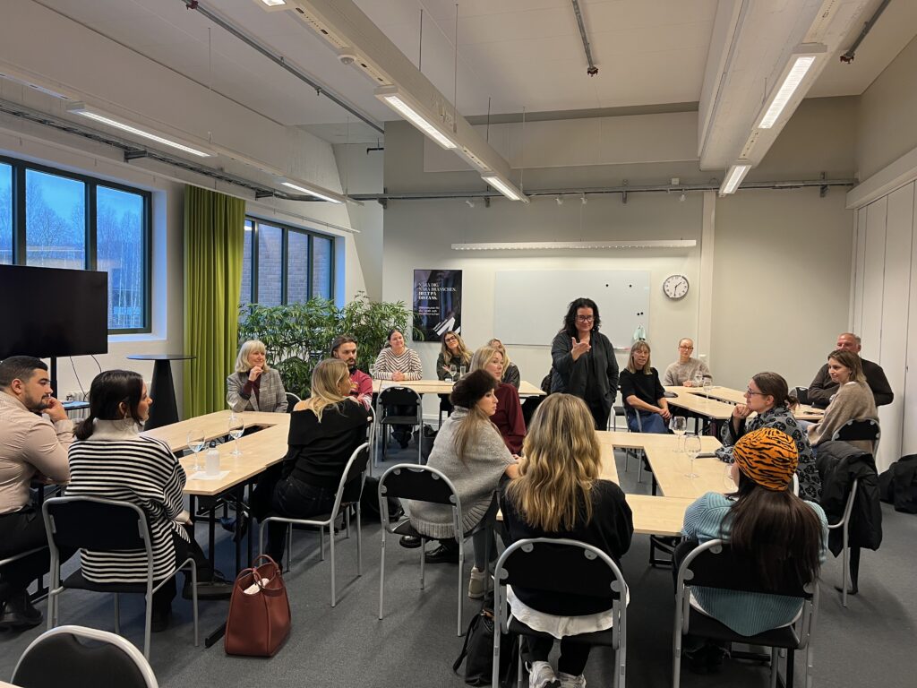 Bild på en grupp av människor som sitter uppdelade vid olika bord i samtal