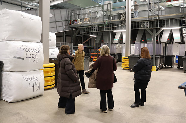 En person pratar inför tre besökare på en anläggning som soretar insamlad textil